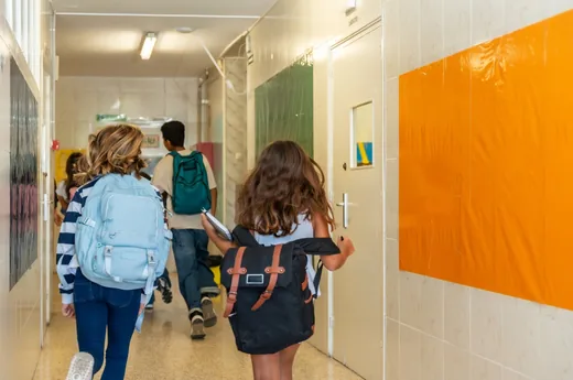 Alunos de costas, com mochilas, caminhando pelo corredor da escola.